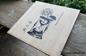 無塗装の縦木目にサンドブラストされた木製看板の中央に砂時計とアジサイのロゴ、ブルーの滴が美しい木の看板