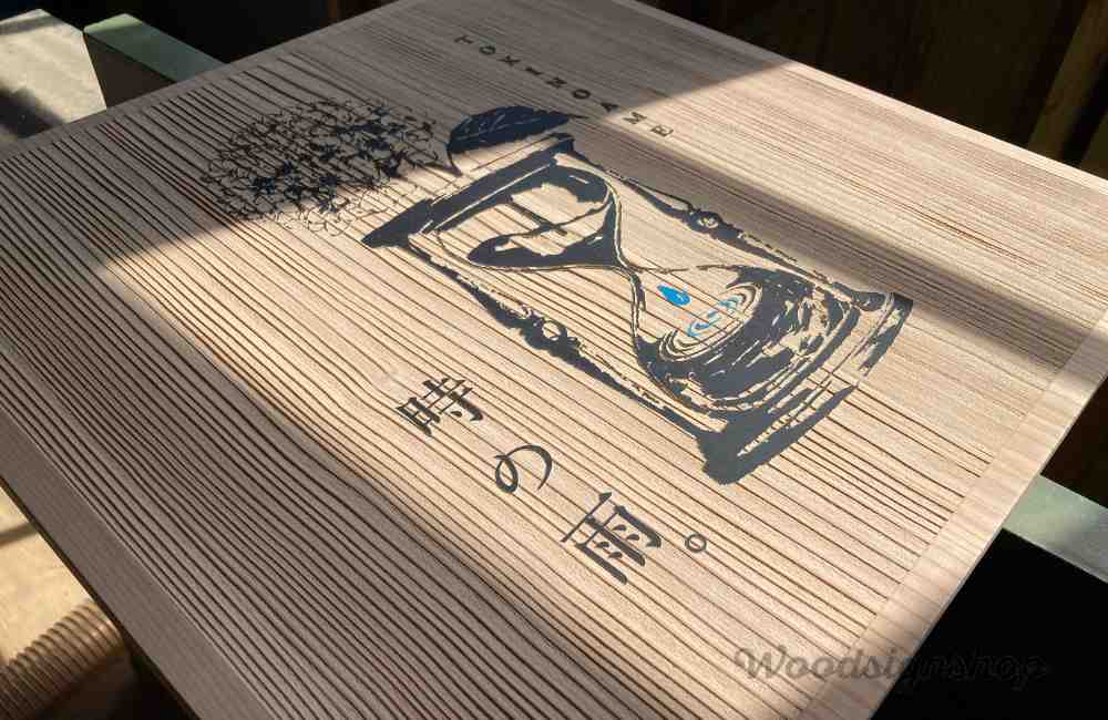 無塗装の縦木目にサンドブラストされた木製看板の中央に砂時計とアジサイのロゴ、ブルーの滴が美しい木の看板