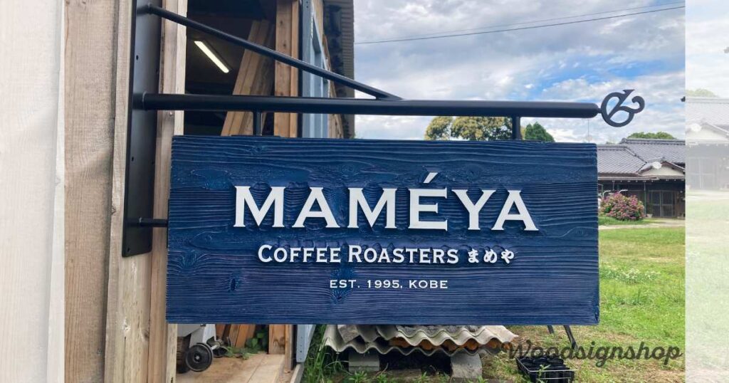 「MAMÉYA Coffee Roasters」の青い木製看板が建物外壁に取り付けられている。白い立体的な文字が映えるデザイン