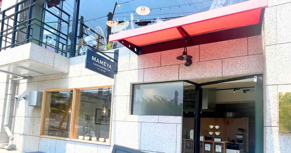 神戸の自家焙煎珈琲店『まめや Coffee Roasters Blend Lab.』の店舗外観と、ウッドサインショップが製作した吊り下げ式の両面木製看板。店舗入口の赤い庇と、壁に設置されたネイビーの看板が印象的。