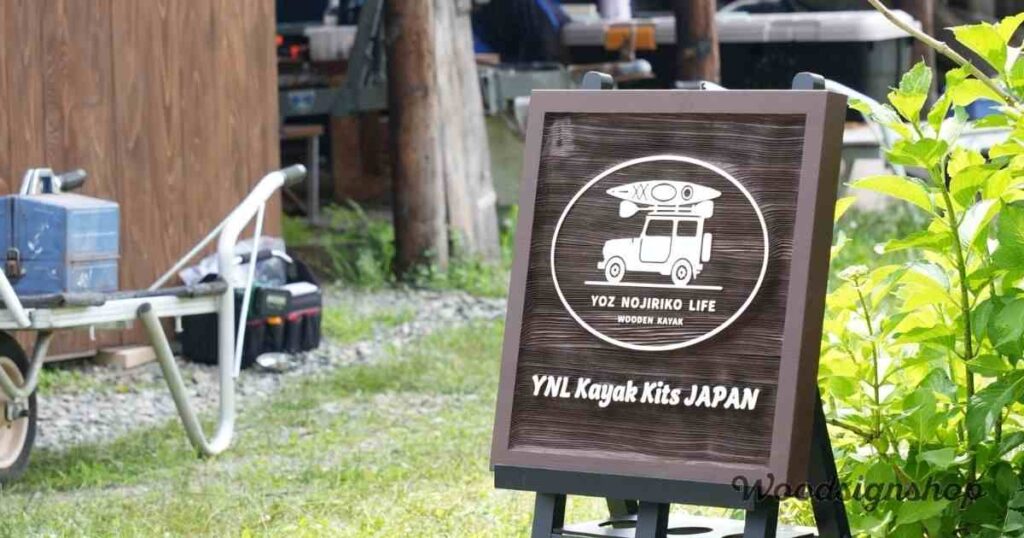 国産杉材で仕上げた木製看板。中央にカヤックを車に載せたロゴと「YOZ NOJIRIKO LIFE WOODEN KAYAK」の文字。下部に「YNL Kayak Kits JAPAN」と記されている。
