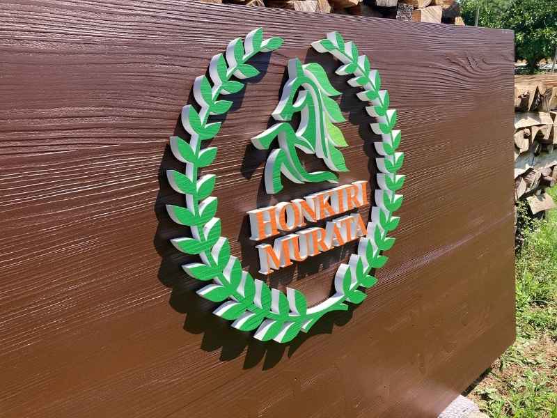 木製看板に取り付けられた、緑色の月桂樹の葉と馬のロゴ、そして白い「HONKIRI MURATA」の立体文字のクローズアップ。