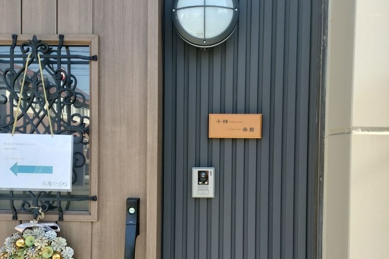 グレーのガルバリウム外壁に設置された、アコヤ材と真鍮ネジの二世帯用木製表札