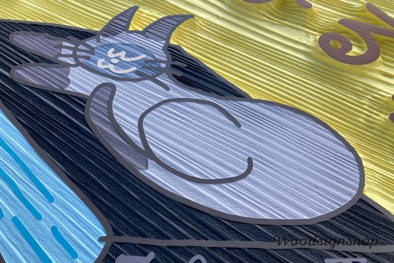 木製看板の浮き彫り細部。サンドブラストによって浮き上がった猫のイラストと本のディテール。