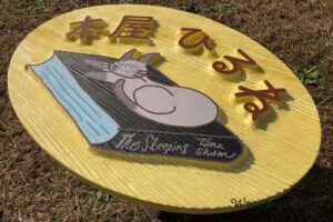 太陽光で強調される木製看板の凹凸質感。サンドブラスト加工で仕上げた「本屋ひるね」の立体サイン。