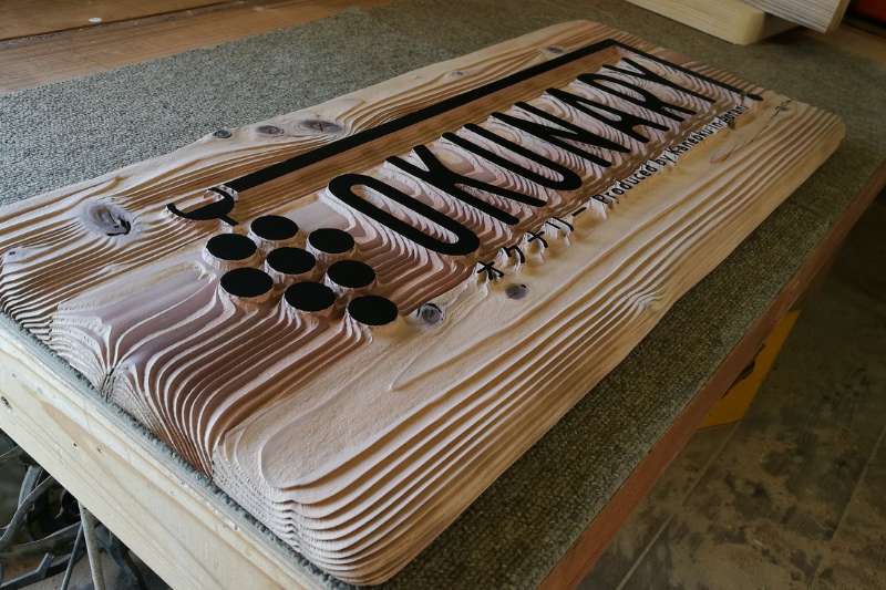 看板の側面から撮影した、重厚な木の厚みと波打つような年輪の重なりが際立つアングル