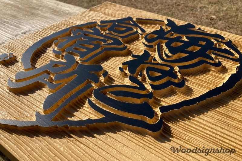 木製看板の接写。木の年輪に沿った凹凸と、丁寧に塗装された黒いロゴ部分のコントラスト。