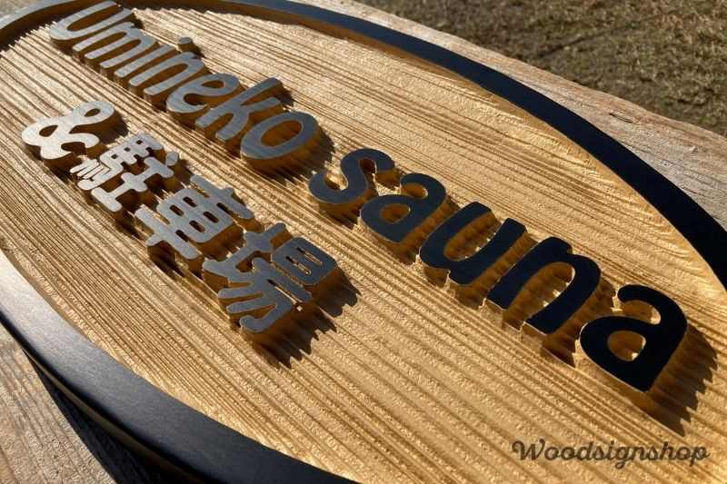 駐車場看板の英文字「Umineko sauna」部分のアップ。立体的な彫りと木目の筋が美しく出ている。