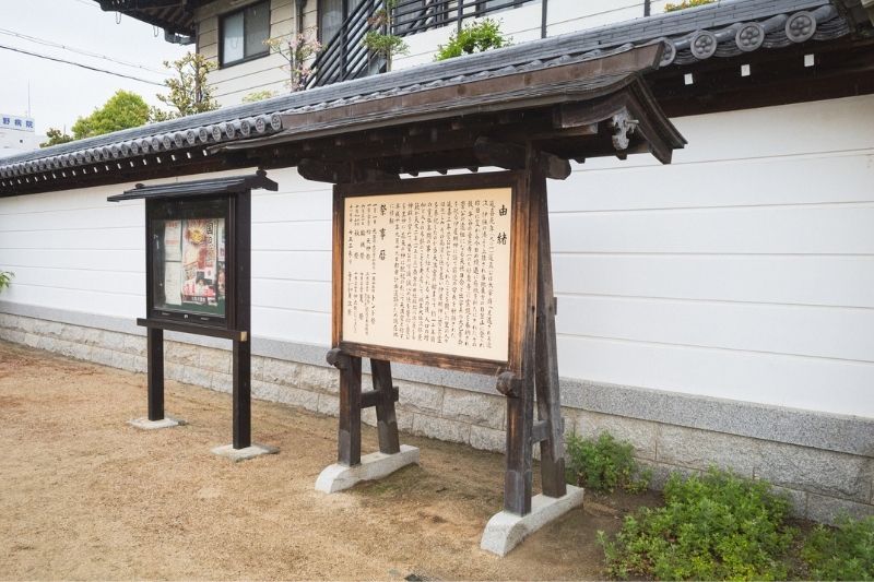 大塩天満宮の厳かな境内の白壁沿いに新しく設置された、屋根付きの木製由緒書き看板の全景