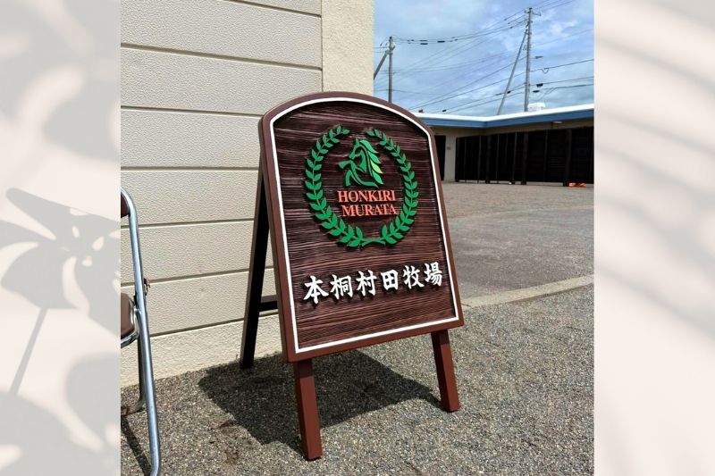 競走馬のセリ会場に設置された、サンドブラスト加工の深い木目と立体ロゴが際立つ本桐村田牧場様の木製A型スタンド看板