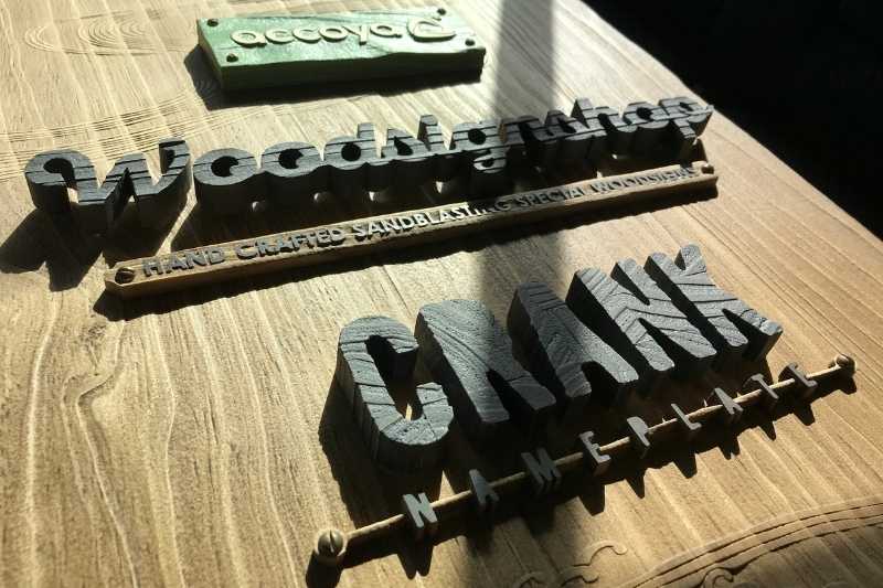木製看板の上に並んだaccoyaの緑のプレート、柾目で作ったWoodsignshopの切り文字、小口を見せたCRANKの切り文字とNAMEPLATEの文字
